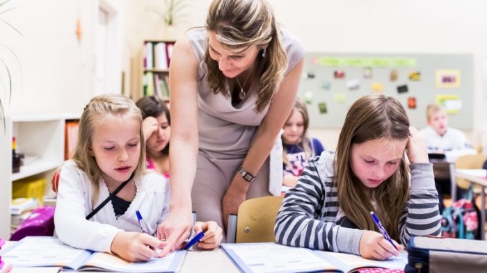 A small school girl sitting at the desk in classroom, looking at camera. A small school girl sitting at the desk in classroom, looking at camera.